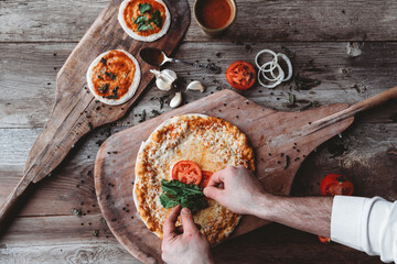 Naklejka premium Hands placing fresh toppings on a homemade pizza