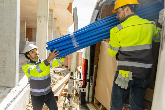 Team of industrial builders passing bundle of blue pipes from truck