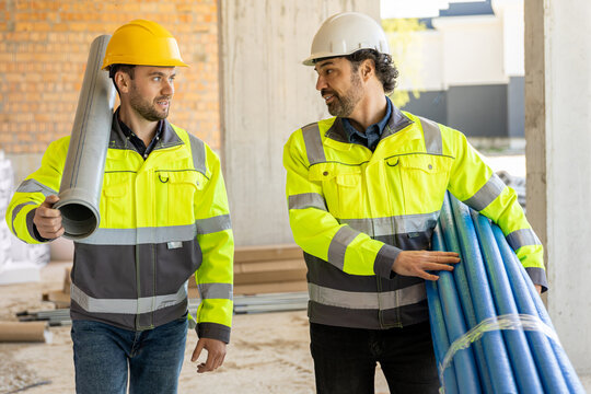 Two multiethnic constructors talking while holding equipment