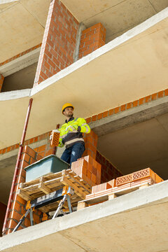 Determined bricklayer standing on scaffolding near wall