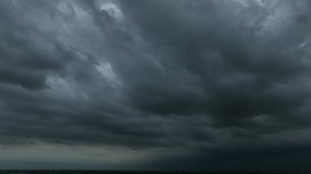 Aerial view of rapidly moving storm clouds covering the sky, showing dark layered formations, turbulent weather patterns, and an intense atmosphere before heavy rainfall reaches the landscape below.
