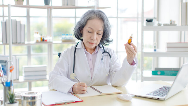 Asian older woman doctor holding drug pill bottle prescription medication dosage medical advice health care consultation in office professional physician treatment services hospital clinic wellness.