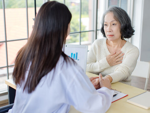 Asian professional female doctor examining senior woman while holding hand for pulse sitting in modern medical office supporting elderly patient during healthcare checkup result healthcare insurance.