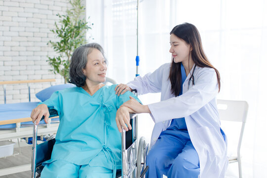 Asian female doctor consulting senior woman patient sitting in wheelchair in hospital clinic attentive comfort support quality elderly healthcare nursing assistance recovery wellness medical services.