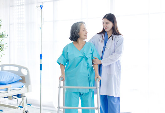 Asian female doctor physical therapist help senior woman walk walker rehabilitation posture therapy in health care clinic professional patient care elderly recovery support wellness medical services.