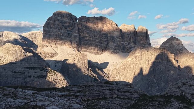 Slow upward drone reveal of Croda dei Toni illuminated by warm golden hour light near Rifugio Lavaredo in the Dolomites, Italy