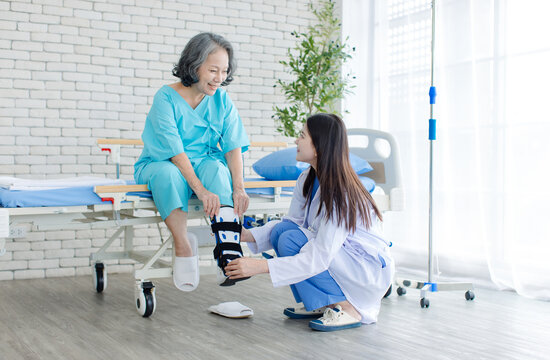 Asian woman healthcare professional fitting orthopedic walking boot on senior patient injured foot during rehabilitation in hospital medical care recovery physical therapy mobility support treatment.