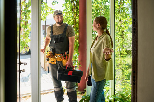 Woman welcoming male technician with toolbox at house entrance. Image represents home maintenance services and is suitable for local repair business marketing