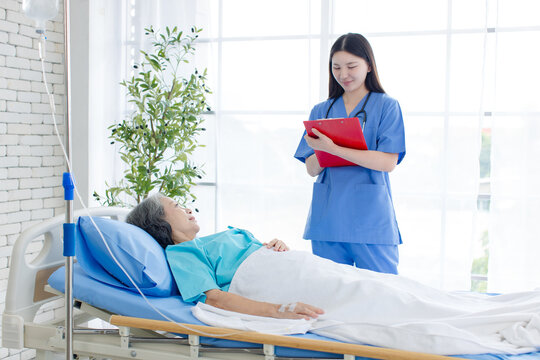 Asian woman nurse visit inquire condition senior female patient resting in hospital bed compassion healthcare support quality elderly  recovery nursing assistance medical treatment wellness services.