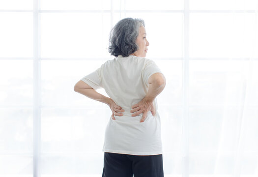 Asian elderly senior woman suffering severe back pain ache arm holding her shoulder on white background symbolizing chronic illness muscle strain repetitive strain injury arthritis aging healthcare.