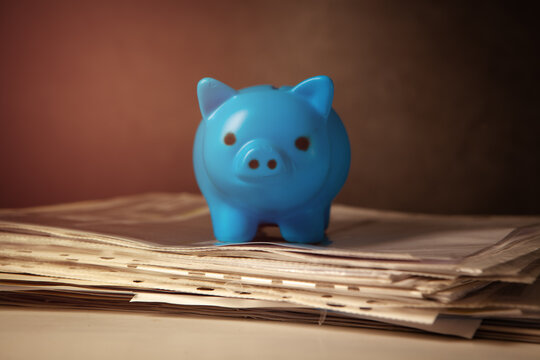 Blue piggy bank on a stack of newspapers. Toned.