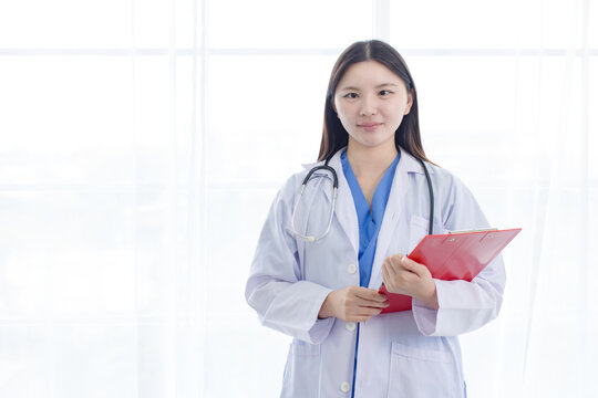 Portrait asian positive young woman doctor wearing white lab coat standing holding prescription folder in hospital clinic office  medical professional represents mission confidence trust patient care.