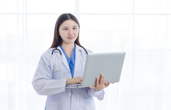Portrait asian positive young woman doctor wearing white lab coat standing holding laptop computer in hospital clinic office  medical professional represents mission confidence trust patient care.