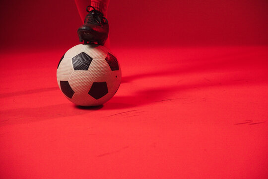 Soccer ball with black cleat and red sock is resting on red seamless floor, copy space