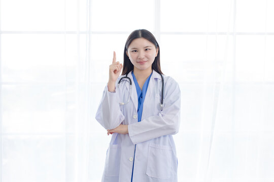 Portrait asian positive young woman doctor wearing white lab coat stethoscope standing post point finger up in hospital clinic medical professional celebration confident healthcare banner advertising.
