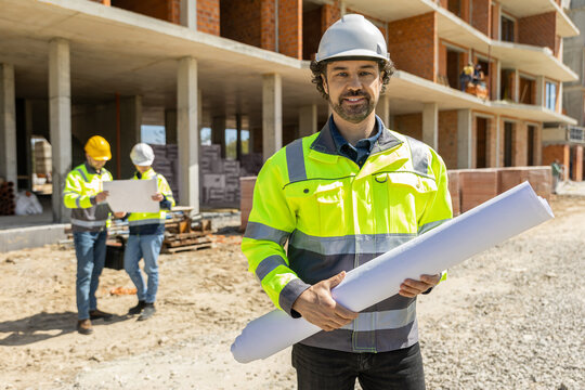 Cheerful male inspector holding rolled document looking at camera
