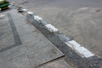 Obraz premium Along the edge of the concrete sidewalk, there are large and small cracks and uneven slabs lining the urban street.