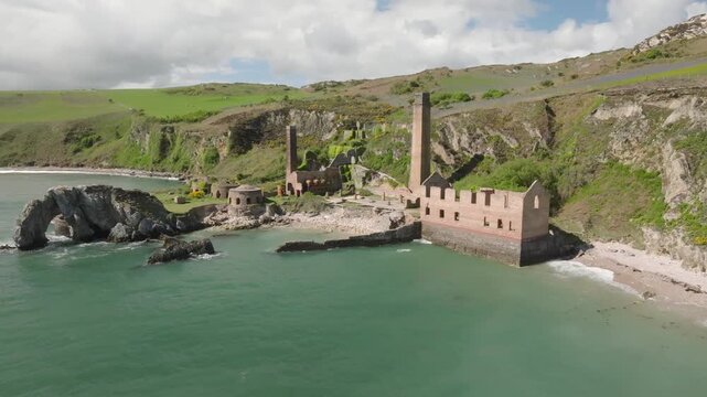 Porth Wen Brickworks, Anglesey, Wales. Slow drone approach over the sea towards derelict buildings, kilns and chimneys.