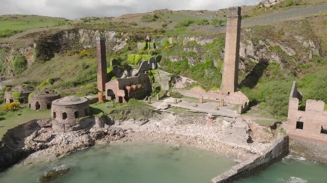 Porth Wen Brickworks, Anglesey, Wales. Industrial Revolution abandoned Victorian site showing beehive kilns and chimneys on sunny day beside the sea.