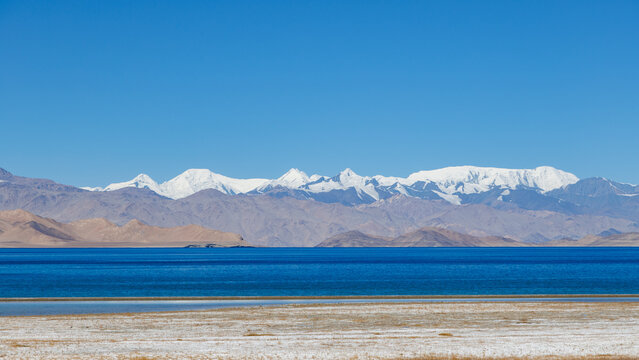 Scenic high-altitude salt lake Karakul with snowy peaks backdrop along Pamir Highway