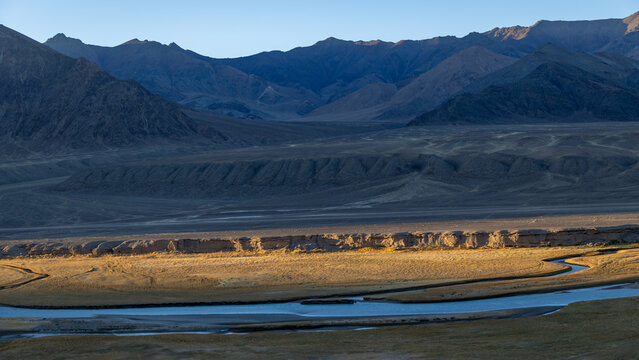 Last golden sunlight illuminating arid plateau and meander river surrounded by dark Pamir mountains
