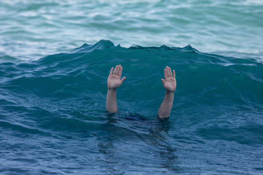 Two hands raised above the water's surface in deep blue ocean waves, evoking urgency and dramatic emotion. Suitable for crisis, rescue, or wellness concepts.