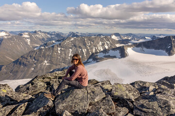 Fototapeta premium Beautiful european family with children and pet dog, hiking Galdhoppigen, 2469 m, the highest mountain peak in Norway on a beautiful sunny summer day, sunset, snow