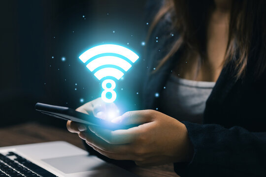 Business professional using smartphone beside laptop with glowing WiFi 8 symbol, illustrating next generation wireless connectivity, fast internet, mobile technology, and digital networking.