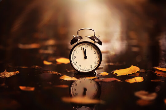 Black alarm clock on colorful maple leaves background. Closeup. Time change concept.