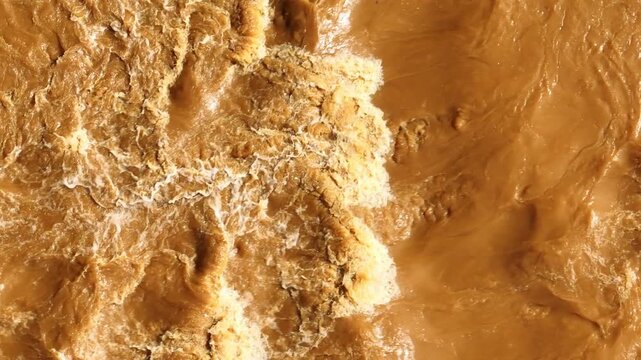 Aerial drone view of powerful muddy flash flood water rushing rapidly with turbulent waves and foamy currents, representing extreme rainfall, natural disasters, and climate change impacts. 4k.
