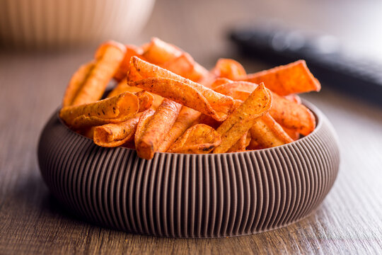 Spicy Corn Snack Chips in Bowl on Wooden Table With TV Remote for Movie Night