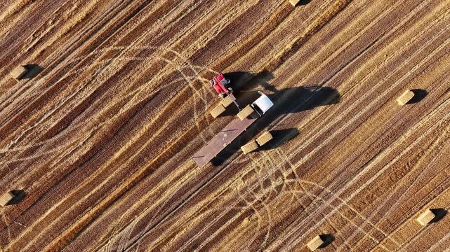 Aerial view of loader loading straw bales onto truck in field at sunset