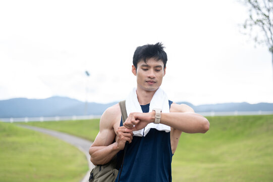 Athletic Asian man checking time on his watch after finished a running workout session in green park