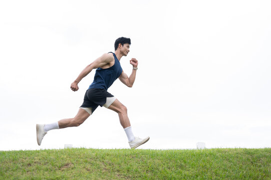 Athletic Asian Man Sprinting Outdoors Across Green Grass