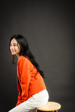 Portrait of a smiling young Southeast Asian Malaysian woman wearing professional corporate attire, featuring a bright orange blazer and black top with a confident pose