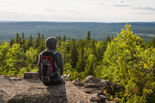 Man with backpack sits on rock overlooking forest