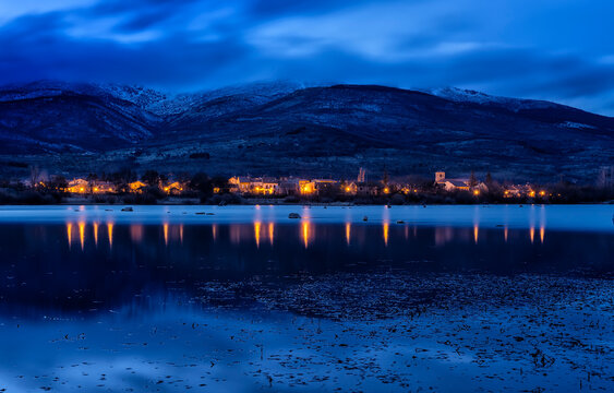 Lakeside Spanish village lights reflect in water at dusk