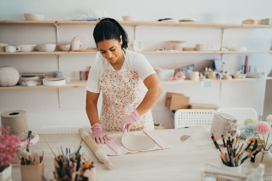 Hispanic Woman in apron shaping clay in pottery studio