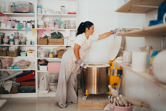 Woman potter carefully loading a ceramic kiln in her studio