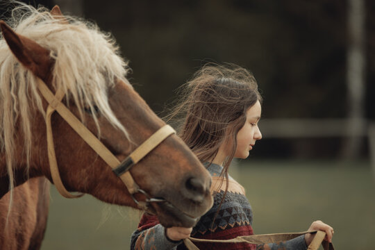 A young girl in a cozy patterned sweater and brown pleated skirt is