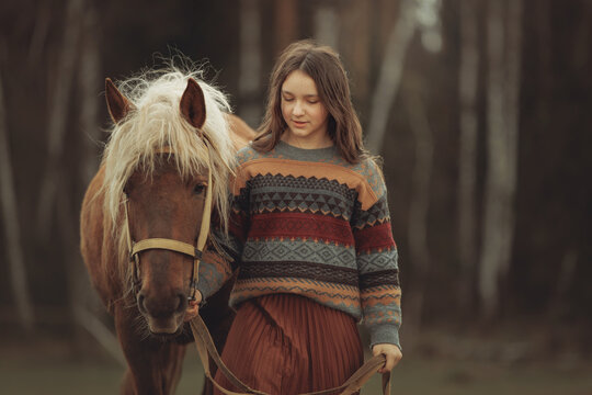 A young girl in a cozy patterned sweater and brown pleated skirt is
