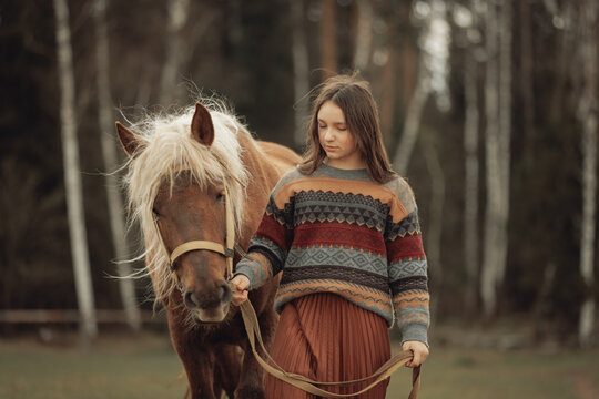 A young girl in a cozy patterned sweater and brown pleated skirt is