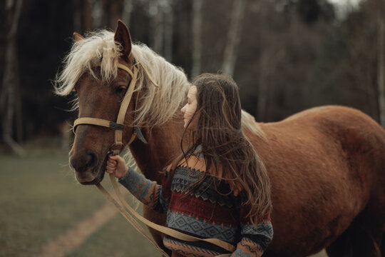 A young girl in a cozy patterned sweater and brown pleated skirt is