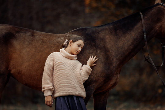 A young girl with a brown horse outdoors in an autumn forest