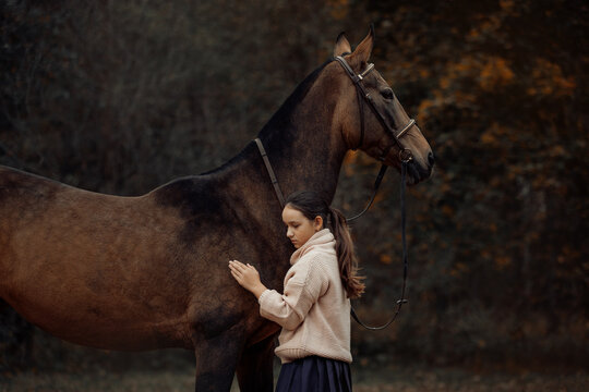 A young girl with a brown horse outdoors in an autumn forest