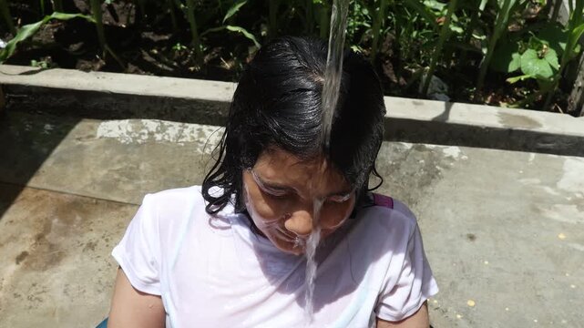 A young girl has water poured over her head by someone else for relief from the intense heat on a hot summer day.