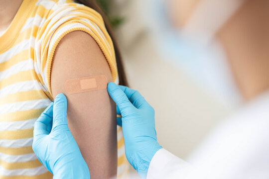 Close up of doctor applying adhesive bandage on girl arm after vaccination.