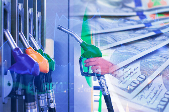 Fuel pump nozzles and a hand holding a green gasoline nozzle over US dollar banknotes with financial charts. Fuel prices, energy costs, oil market and inflation concept for business finance.