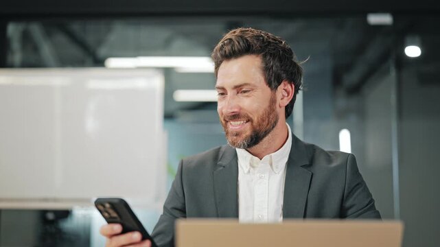 Professional engages with digital devices. Individual smiles, conveying contentment with digital communication and productivity in office environment.