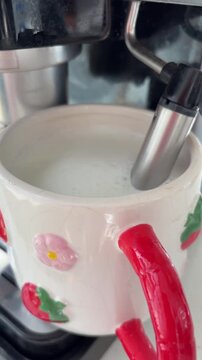 Coffee machine steam wand frothing milk in a ceramic mug for making a morning cappuccino, creating a creamy foam for a delicious hot beverage and a perfect breakfast routine